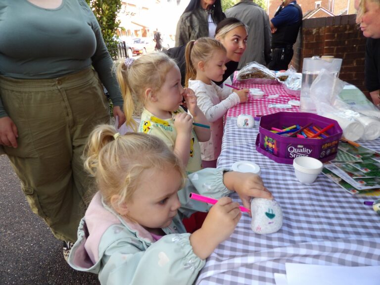 Children decorating cups at a craft table with adults helping