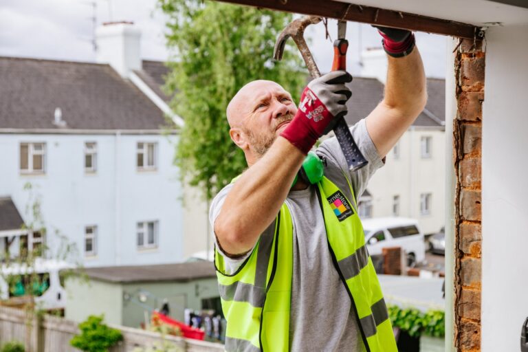 An operative in a hi-vis vest working overhead on a doorway during a repair
