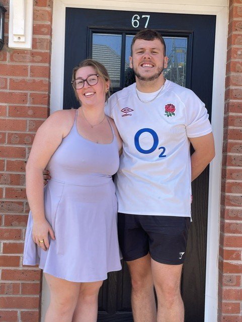 A couple standing outside the front door of their new home, number 67