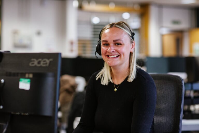 A Cornerstone colleague wearing a headset at her desk in an open plan office