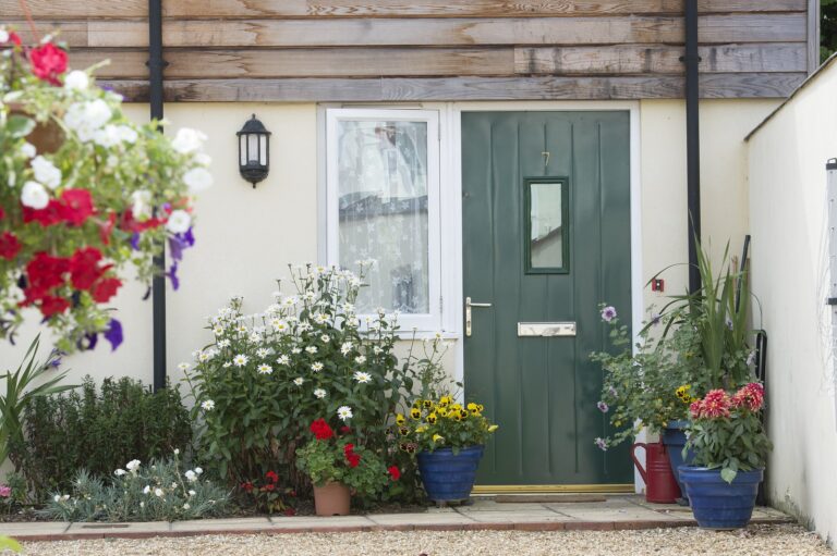 The front door of a home with hanging baskets and pots of flowers on either side