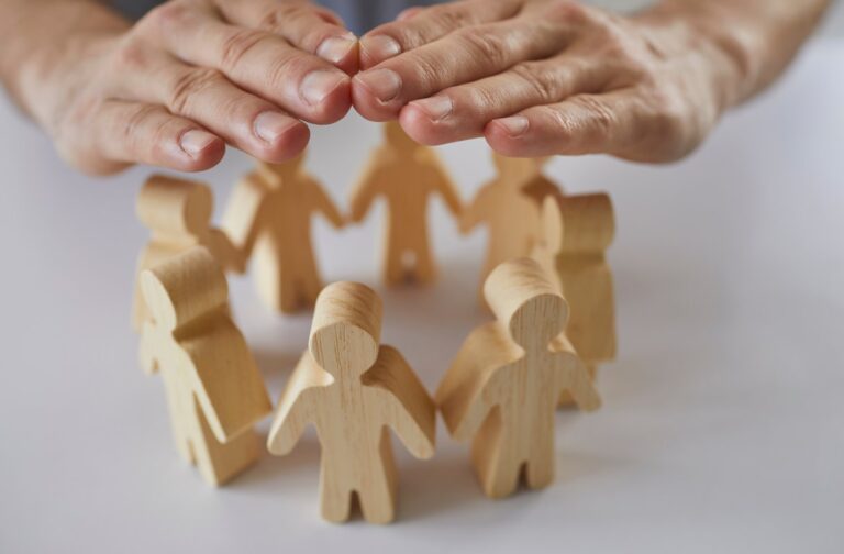 A pair of hands held protectively above a circle of small wooden figures