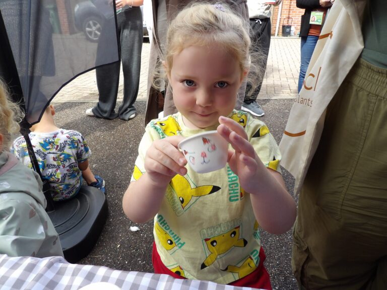 A young girl holds up a cup she has decorated at an outdoor community event
