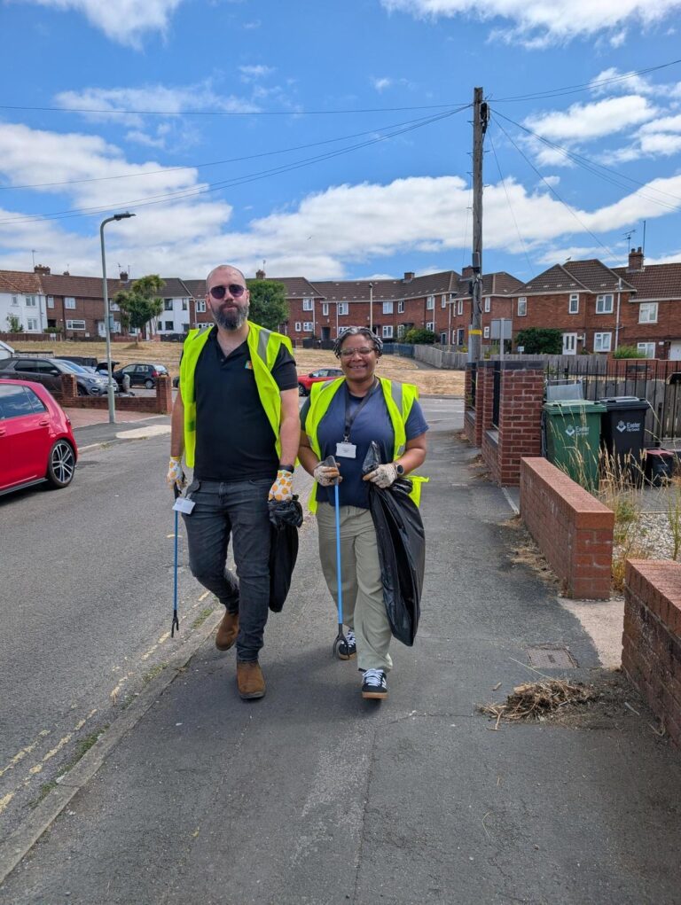 Two people in hi-vis vests litter picking along a residential street