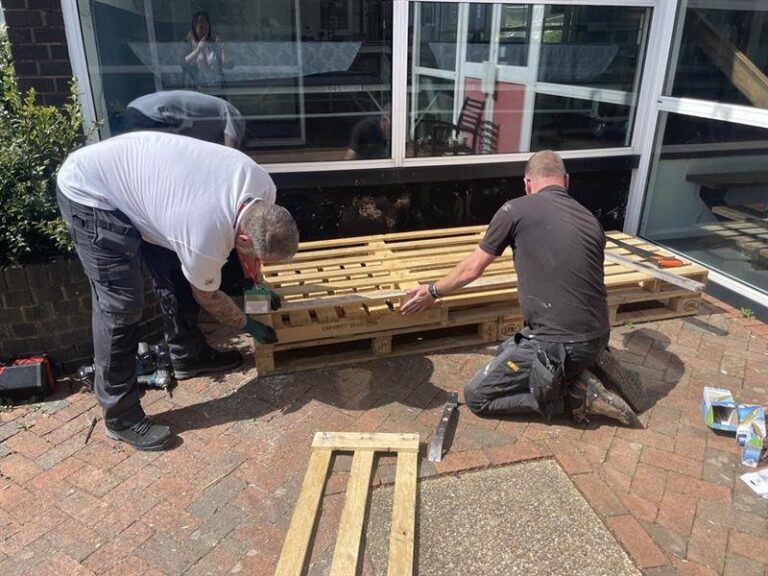 Two people building a timber seating structure on a patio