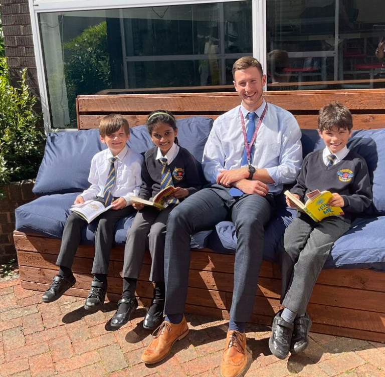 A Cornerstone colleague sitting outdoors reading with four schoolchildren